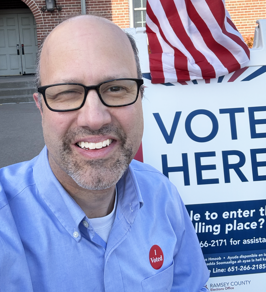 Representative Dave Pinto at voting locating in front of American flag and "Vote Here" sign - Retouched photo